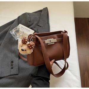 Detail of brown litchi pattern leather shoulder bag with a silver lock and bear charm