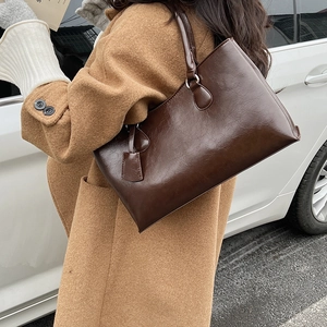 Close-up of deep brown glossy tote bag with silver hardware on model in camel coat