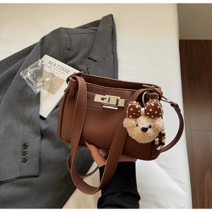 Detail of brown litchi pattern leather shoulder bag with silver metal swivel lock and plush bear