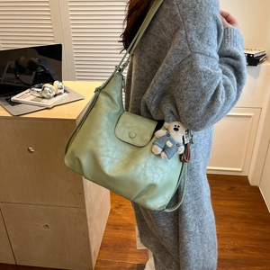 Detail of mint green soft leather crossbody bag with a magnetic buckle and bear pendant