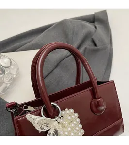 Close-up of wine red glossy leather handbag with pearl strap and bow detail