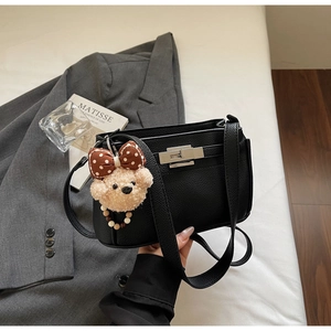 Detail of black lychee grain leather handbag with silver lock and plush teddy bear charm