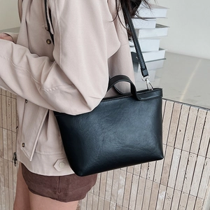 Detail of a black matte leather tote bag featuring sleek handles and a slim shoulder strap