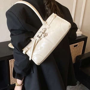 Détail d'un sac à bandoulière en cuir blanc cassé avec boucles argentées porté par un modèle