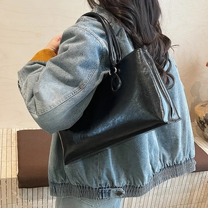 Side view of black glossy patent leather tote bag carried on shoulder with denim jacket