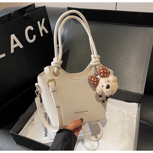Detailed view of white litchi pattern bucket bag with woven handles and bear charm