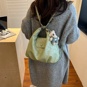 Detail of light green PU leather backpack featuring a cute plush bear pendant accessory