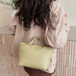 Green leather tote bag worn by a model showcasing its large capacity and modern minimalist style