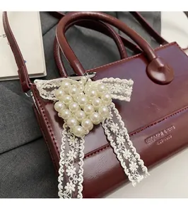 Detail of white pearl heart charm with floral lace ribbon on burgundy leather bag
