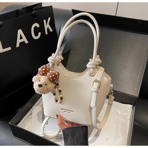 Close-up of white lychee leather bucket bag with knotted handle and plush bear charm