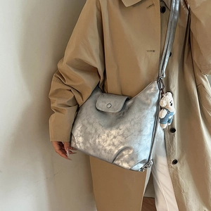 Detail of silver metallic tote bag with bear charm pendant on stylish beige trench coat