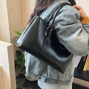 Side view of a black glossy leather tote bag worn by a model in a cozy home setting