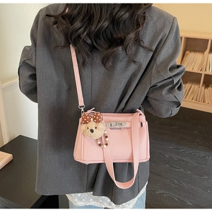 Detail view of pink lychee grain shoulder bag with silver turn-lock and plush bear charm