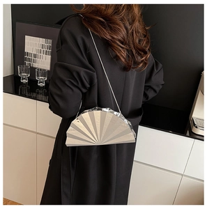 Silver shell-shaped metallic crossbody bag with chain strap styled on a black coat