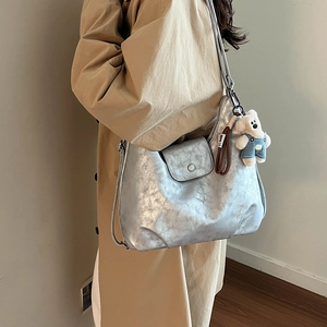 Detail of silver PU leather tote bag with metallic texture and white plush bear charm