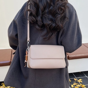 Dettaglio della piccola borsa a tracolla beige con trama a grana e nappa di perline in legno