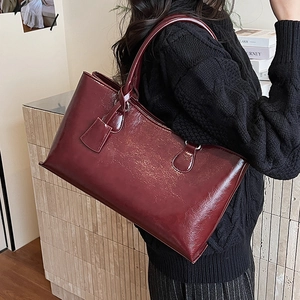 Detail of burgundy leather tote bag with glossy finish shown on model's shoulder