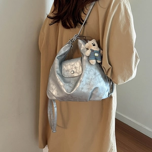 Silver metallic tote bag with buckle flap and teddy bear charm on khaki trench coat