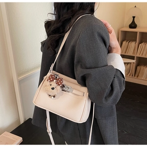 Detail of beige textured leather handbag with a plush puppy charm and metal buckle