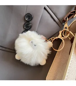Close-up of a white fluffy faux fur keychain charm with gold metal clasp on a beige bag