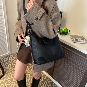 Model wearing a black large capacity leather shoulder bag with white bear keychain