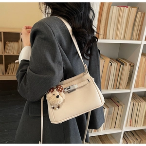 Detail of beige lychee leather shoulder bag with silver clasp and plush bear charm