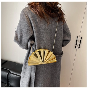 Detailed view of glossy gold shell clutch bag with metallic chain on long gray wool coat