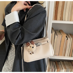 Detail of off-white lychee grain leather bag with silver lock and plush bear charm