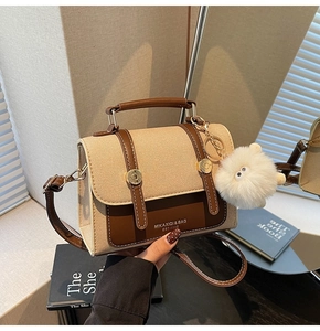 Detail of a vintage beige canvas crossbody bag with brown leather trim and a white plush charm