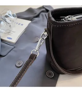 Détail du crochet en métal argenté et des surpiqûres blanches sur un sac seau en cuir marron