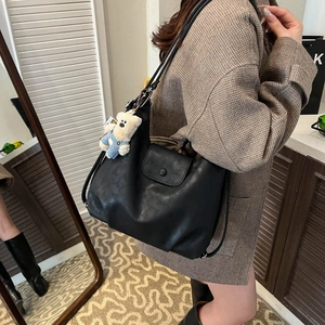 Detail of minimalist black PU leather tote bag with cute plush bear charm accessory