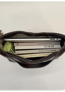 Spacious interior of dark brown leather tote bag holding a laptop books and umbrella