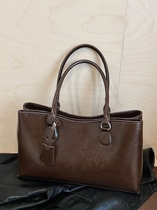 Elegant dark brown leather tote bag with long handles and decorative tag on dark surface