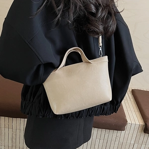 Mid-shot of a cream leather tote bag shown from the side on a model in a minimalist room