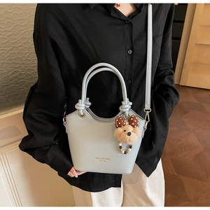 Detail of light blue bucket bag with plush bear charm and leather texture on a model
