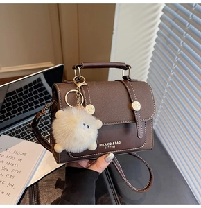 Detail of vintage brown textured leather crossbody bag with golden buckles and plush charm