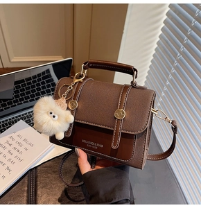 Detailed view of brown leather crossbody bag with fuzzy monster charm and office accessories