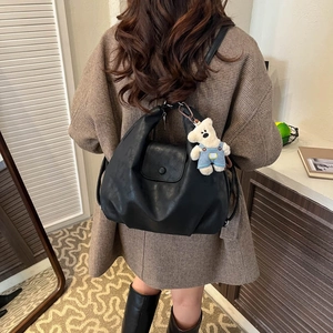 Close-up of black PU leather backpack with a cute teddy bear charm on plaid wool coat