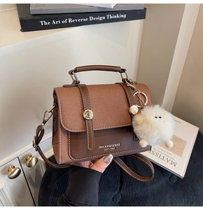 Detail of a brown lychee pattern leather crossbody bag with golden buckles and plush charm