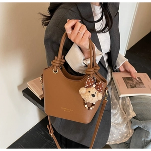 Detail of brown litchi pattern bucket bag with knot handle and plush bear charm decoration