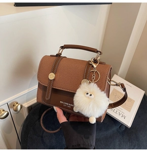 Detail of a brown leather crossbody bag with vintage gold buckle and plush ball charm