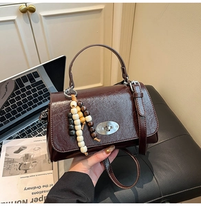 Detail of burgundy vintage square bag with glossy texture, oval lock, and wooden beads