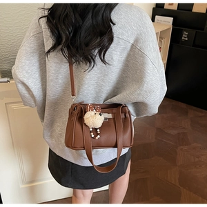 Close-up of brown pebbled leather handbag with silver square buckle and cute teddy bear charm