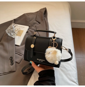 Close-up of black crossbody bag with white stitching and plush sheep pendant detail