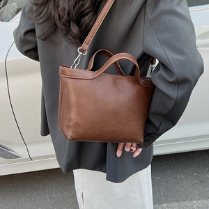 Brown leather tote bag worn as a shoulder bag by a model in a casual street style look