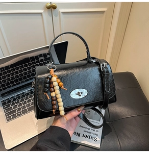 Detail of black wrinkled leather handbag with silver twist lock and colorful beaded charm