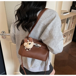 Detail of brown lychee grain leather handbag featuring silver twist lock and bear charm