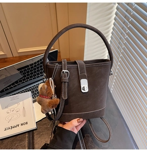 Détail d'un sac seau marron foncé avec boucle argentée et accessoire de charme ours en peluche