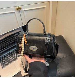 Close-up of black glossy handbag with silver oval twist lock and wooden bead charms