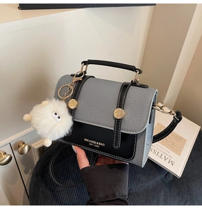 Detail of grey crossbody bag with monster fur charm and gold hardware on a table